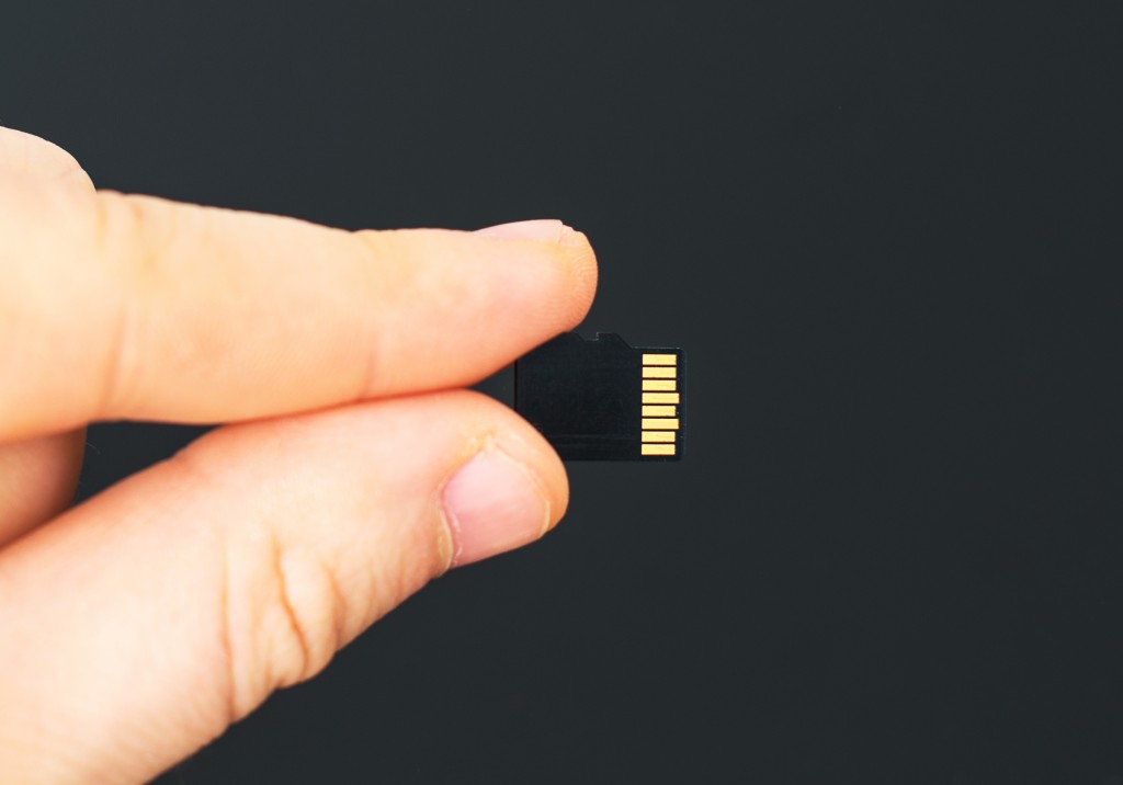 Male hand holding Micro SD card on black background.